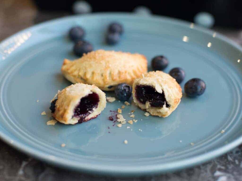 two blueberry hand pies with flaky crust and homemade blueberry pie filling on a blu plate