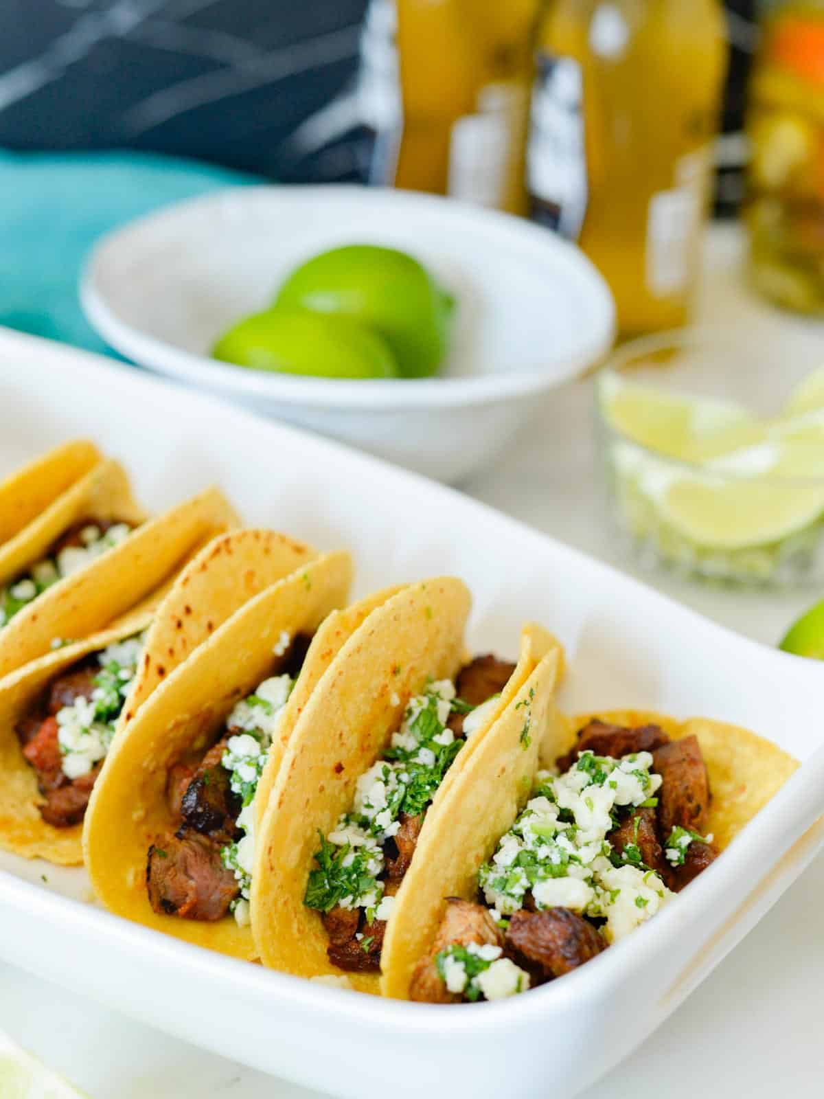 carne asada tacos served at a cookout with fresh limes and cotija cheese