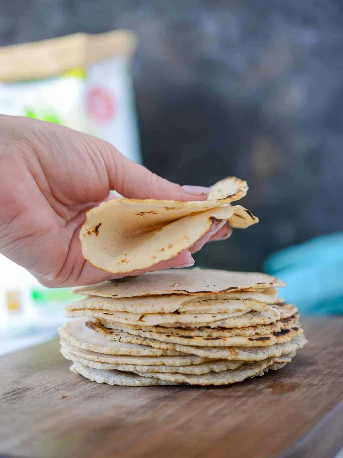 a stack of homemade corn tortillas in a hand showing their flexibility