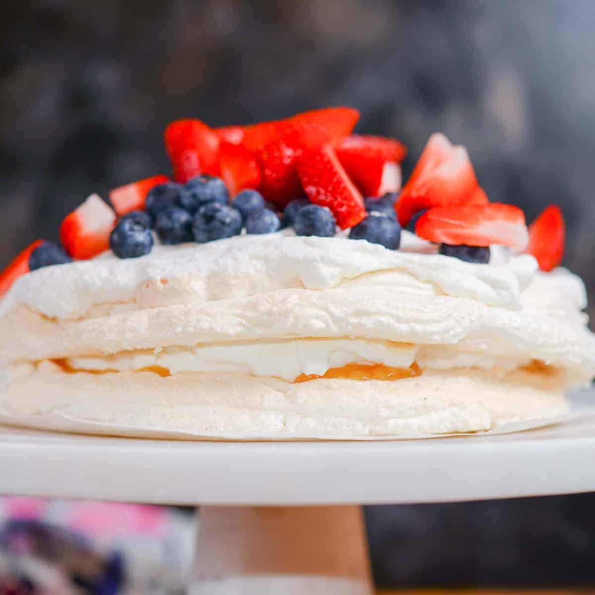 pavlova cake with lemon curd and fresh whipped cream presented on a marble cake stand