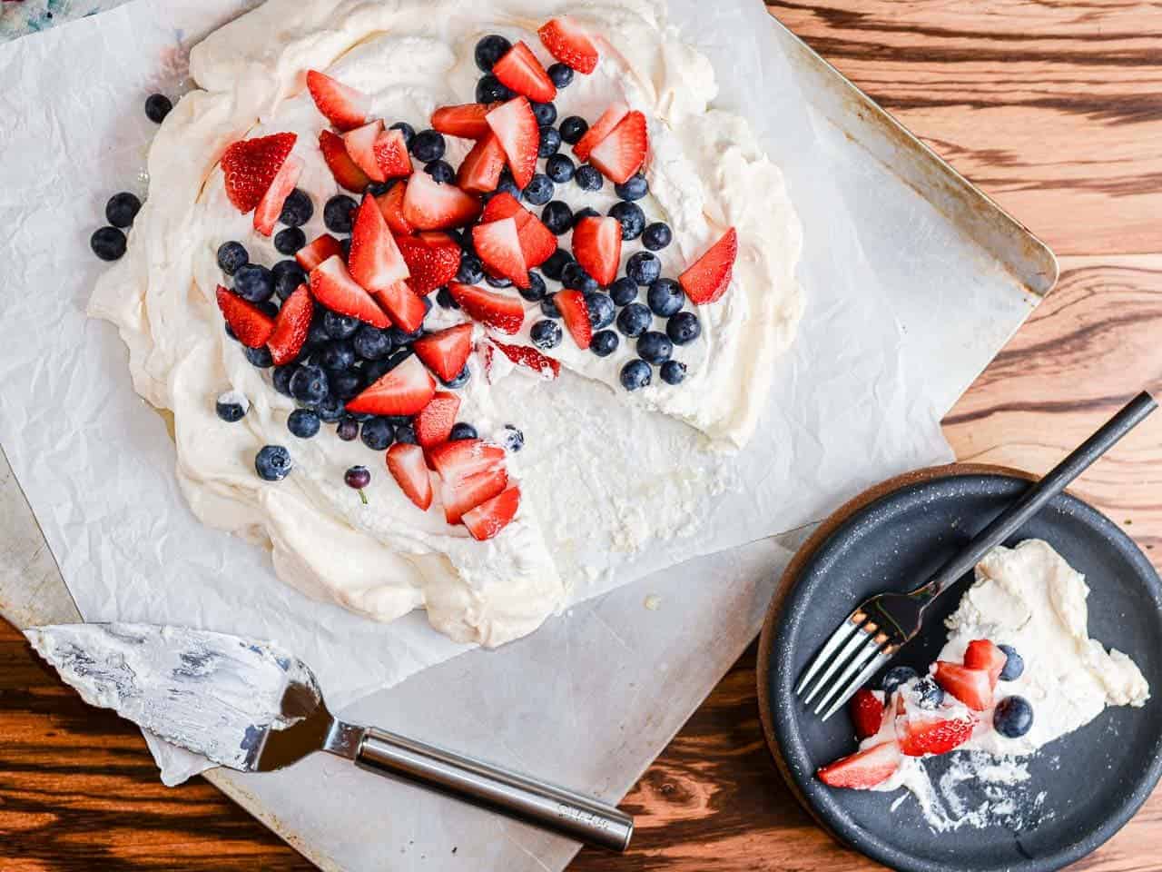 summer pavlova recipe topped with whipped cream and fresh strawberries and blueberries