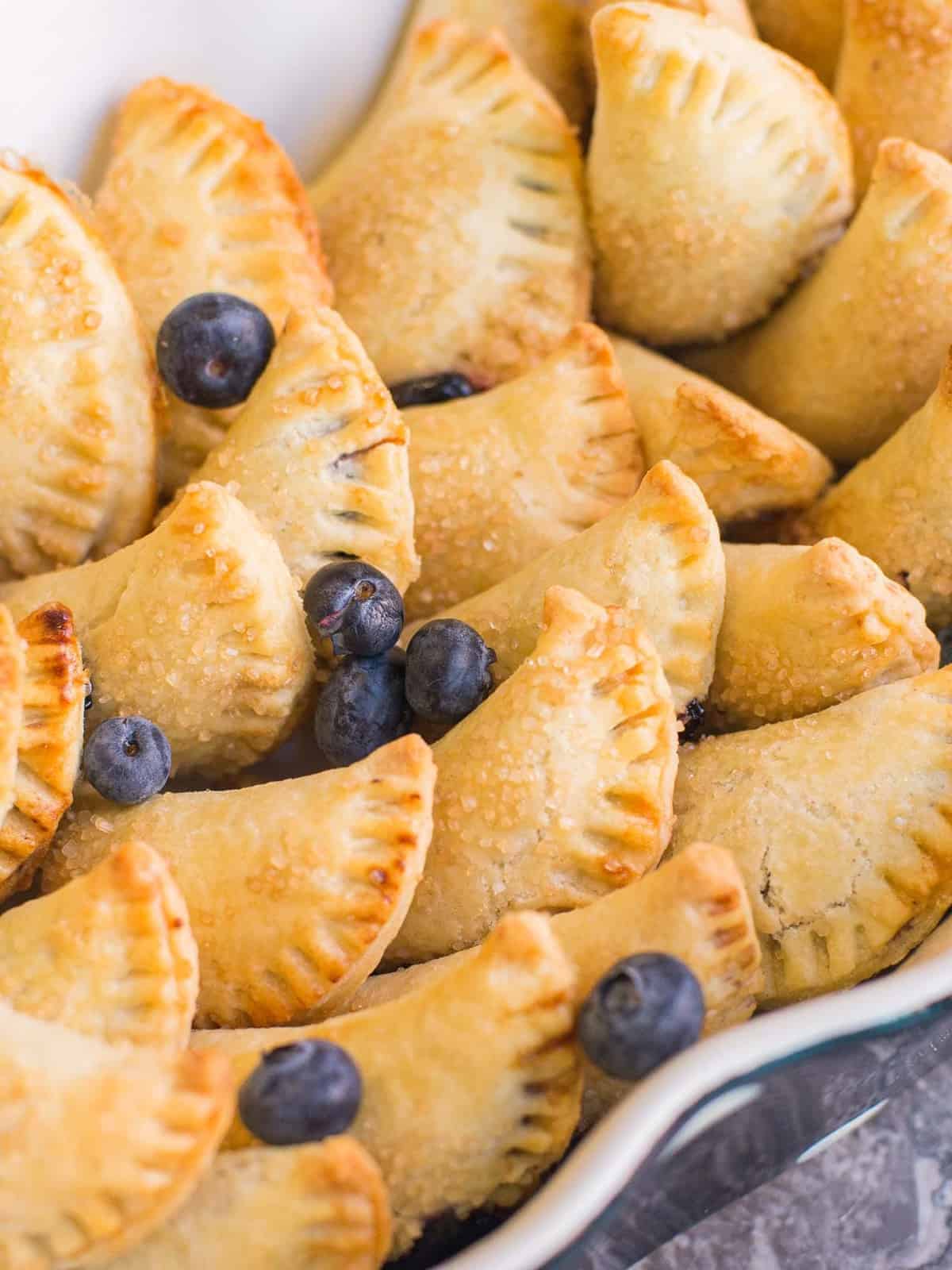 a tray full of homemade blueberry hand pies, topped with a few fresh blueberries