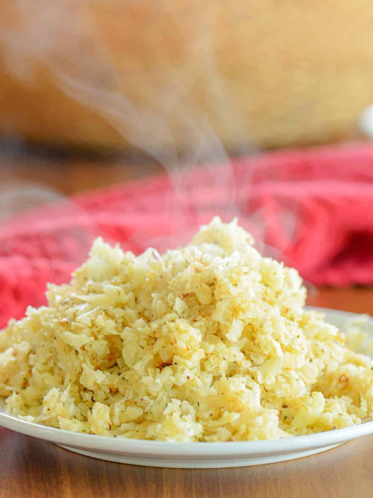 the best homemade cauliflower rice steaming on a plate with butter and herb seasonings
