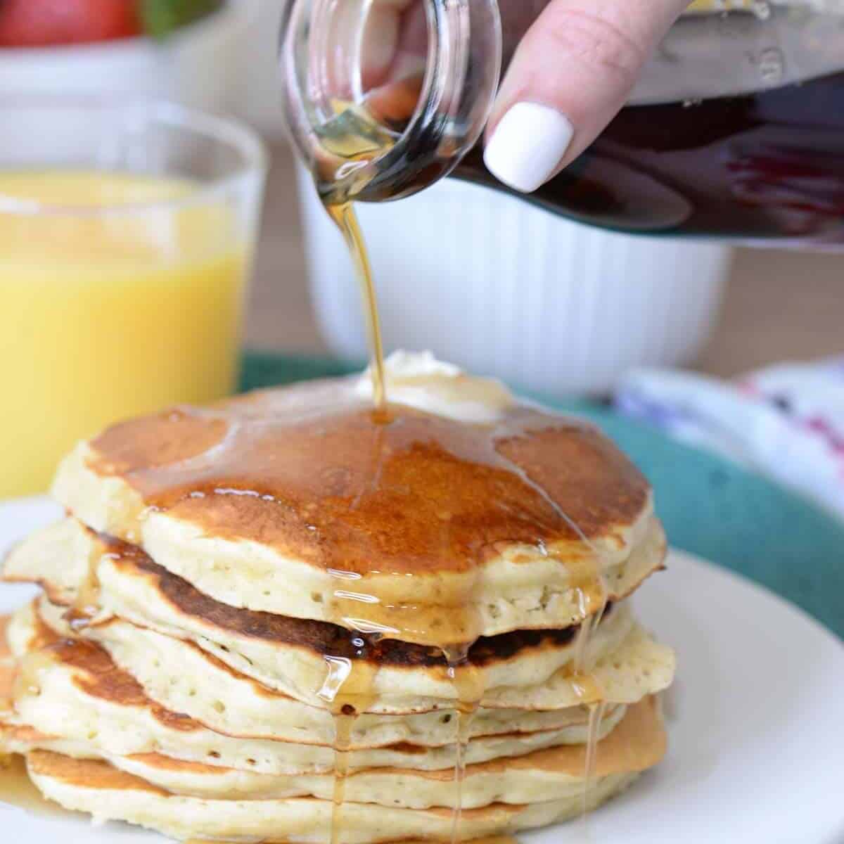 a stack of buttermilk pancakes with syrup being poured over