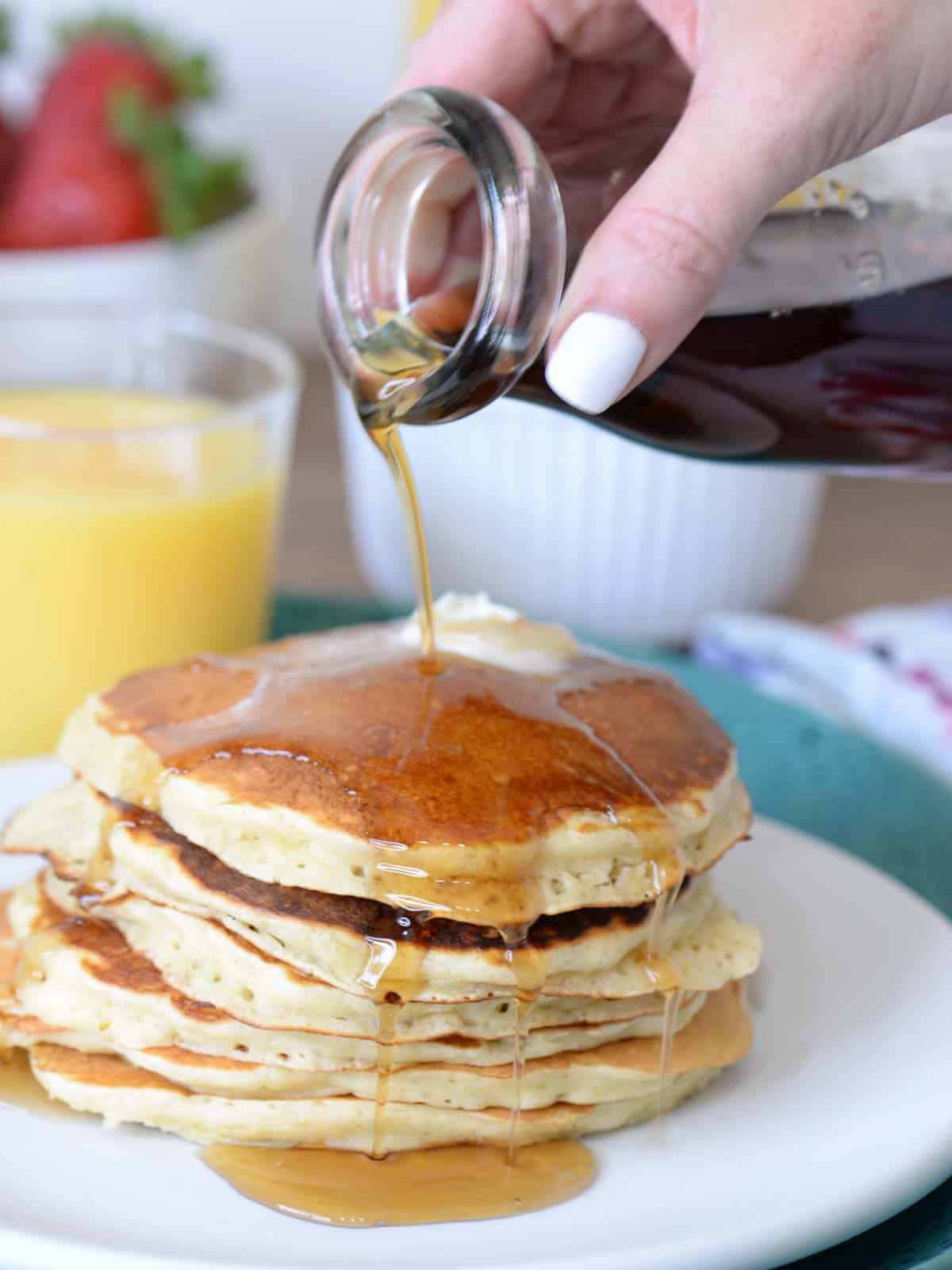 a stack of buttermilk pancakes with syrup being poured over