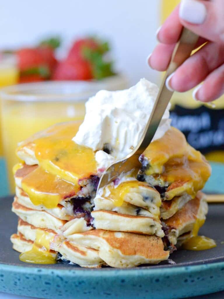 Stack of blueberry pancakes with lemon curd and whipped cream