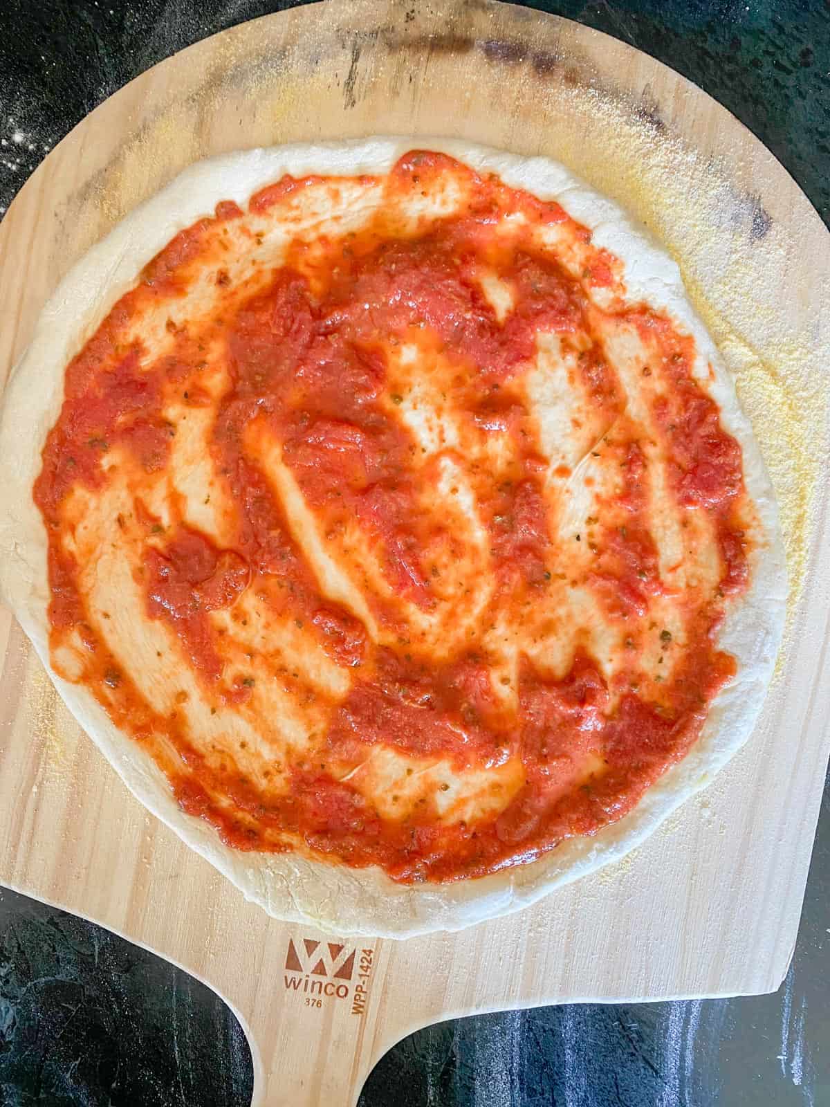 homemade pizza sauce on pizza dough on a pizza peel