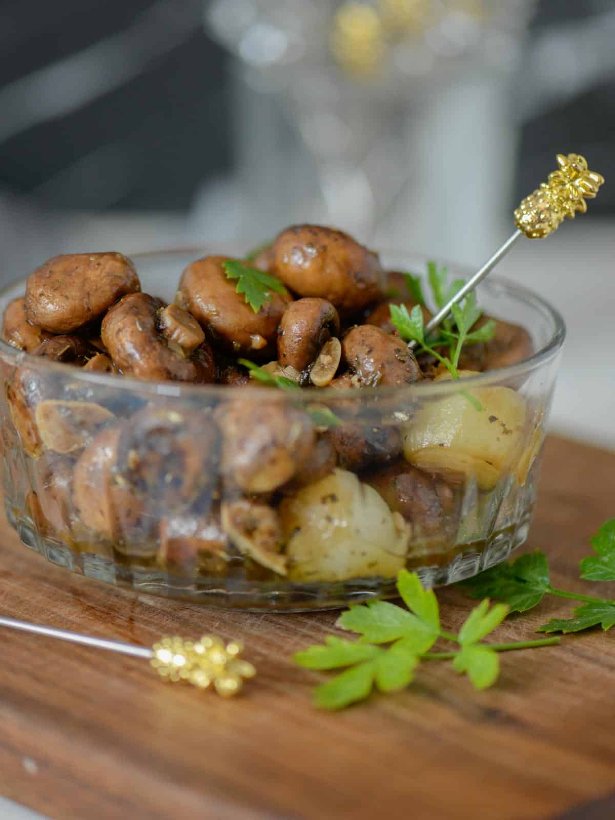 A bowl of mushrooms marinated in Italian seasonings and served with cocktail picks.