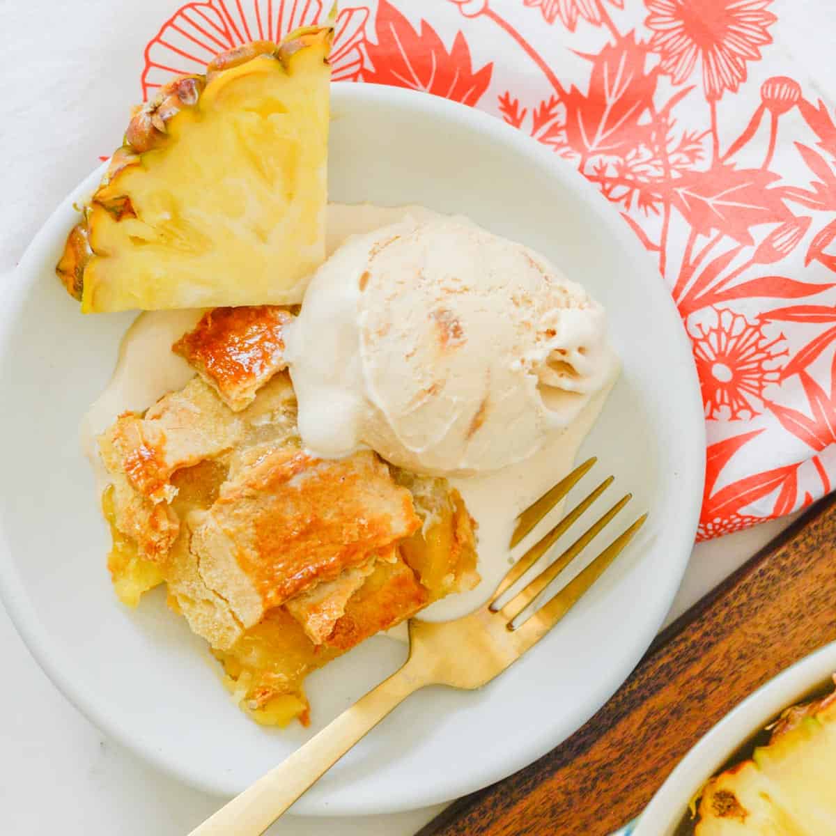 a slice of pineapple pie served with ice cream and a fresh pineapple