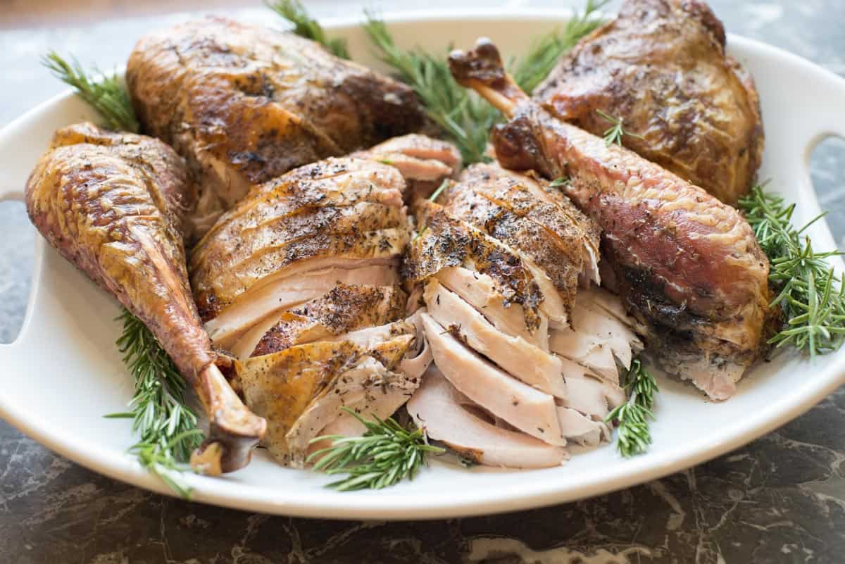 carved thanksgiving turkey on a white platter with fresh herbs