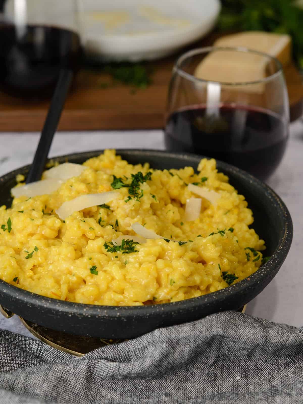 easy risotto in a black dish with a glass of red wine and grated parmesan