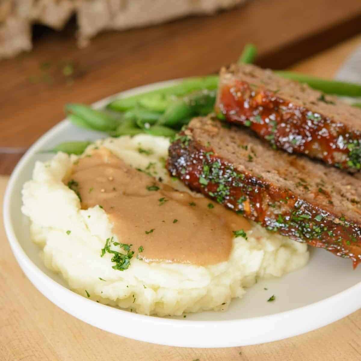 Meatloaf recipe served with mashed potatoes topped with gravy and blanched green beans