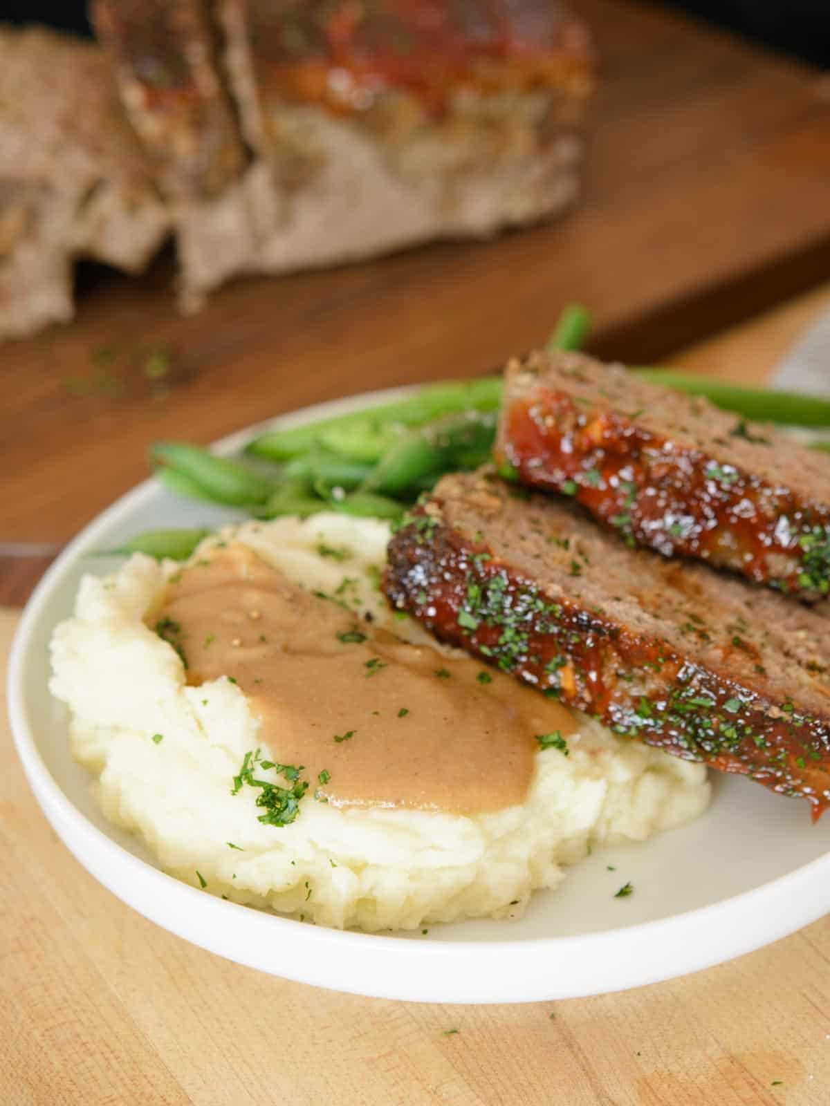 Meatloaf recipe served with mashed potatoes topped with gravy and blanched green beans