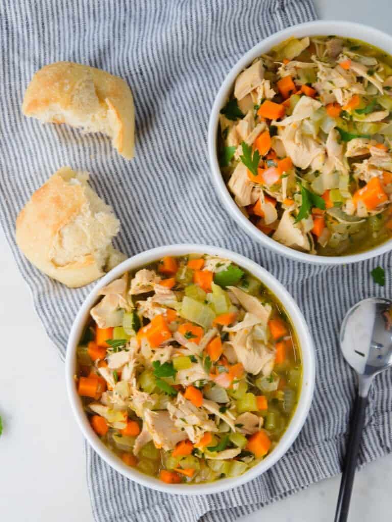 two bowls of homemade turkey soups served with dinner rolls