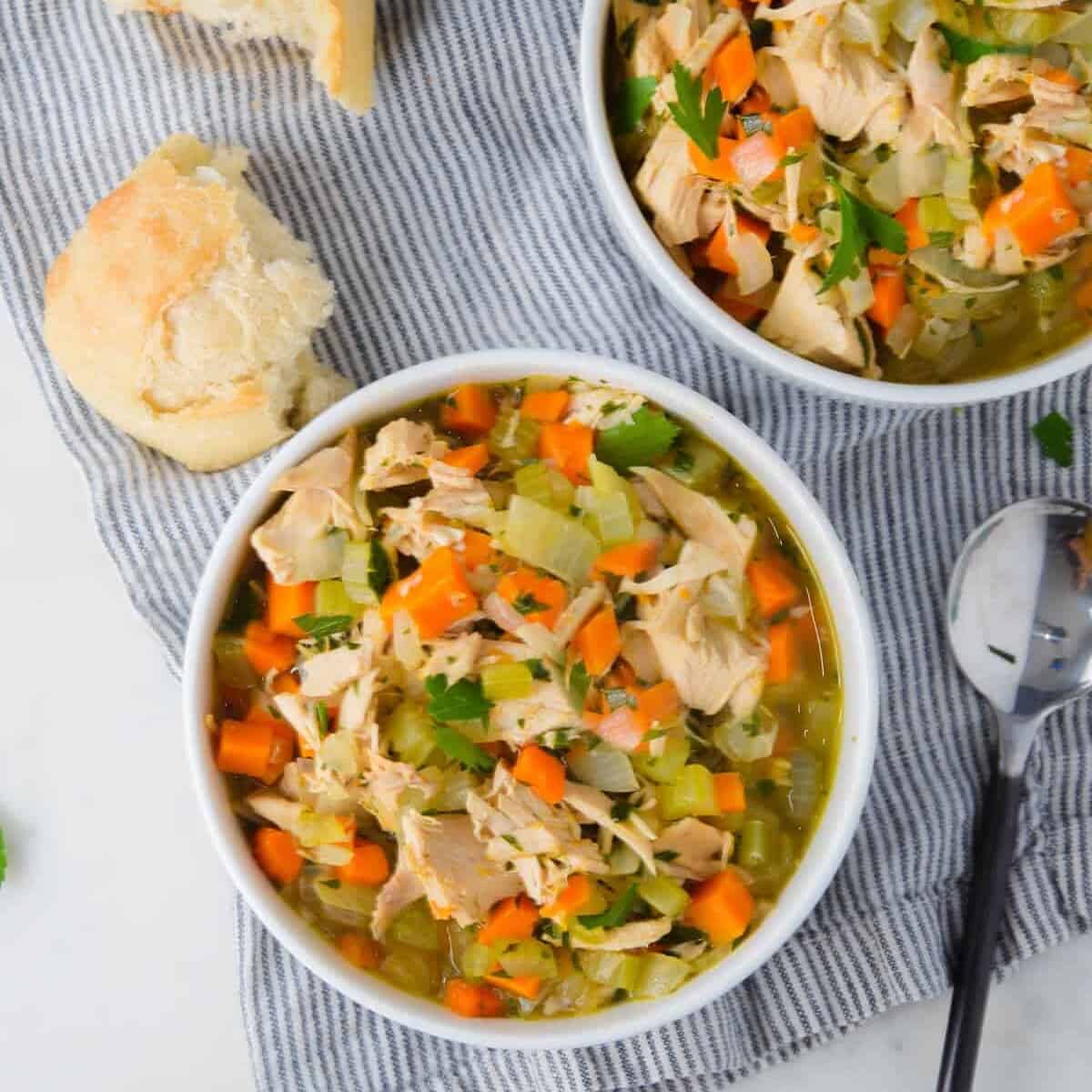 two bowls of homemade turkey soups served with dinner rolls