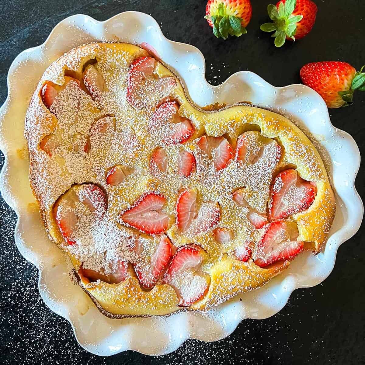 strawberry clafoutis recipe from scratch in a heart shaped pie dish with fresh strawberries sprinkled around