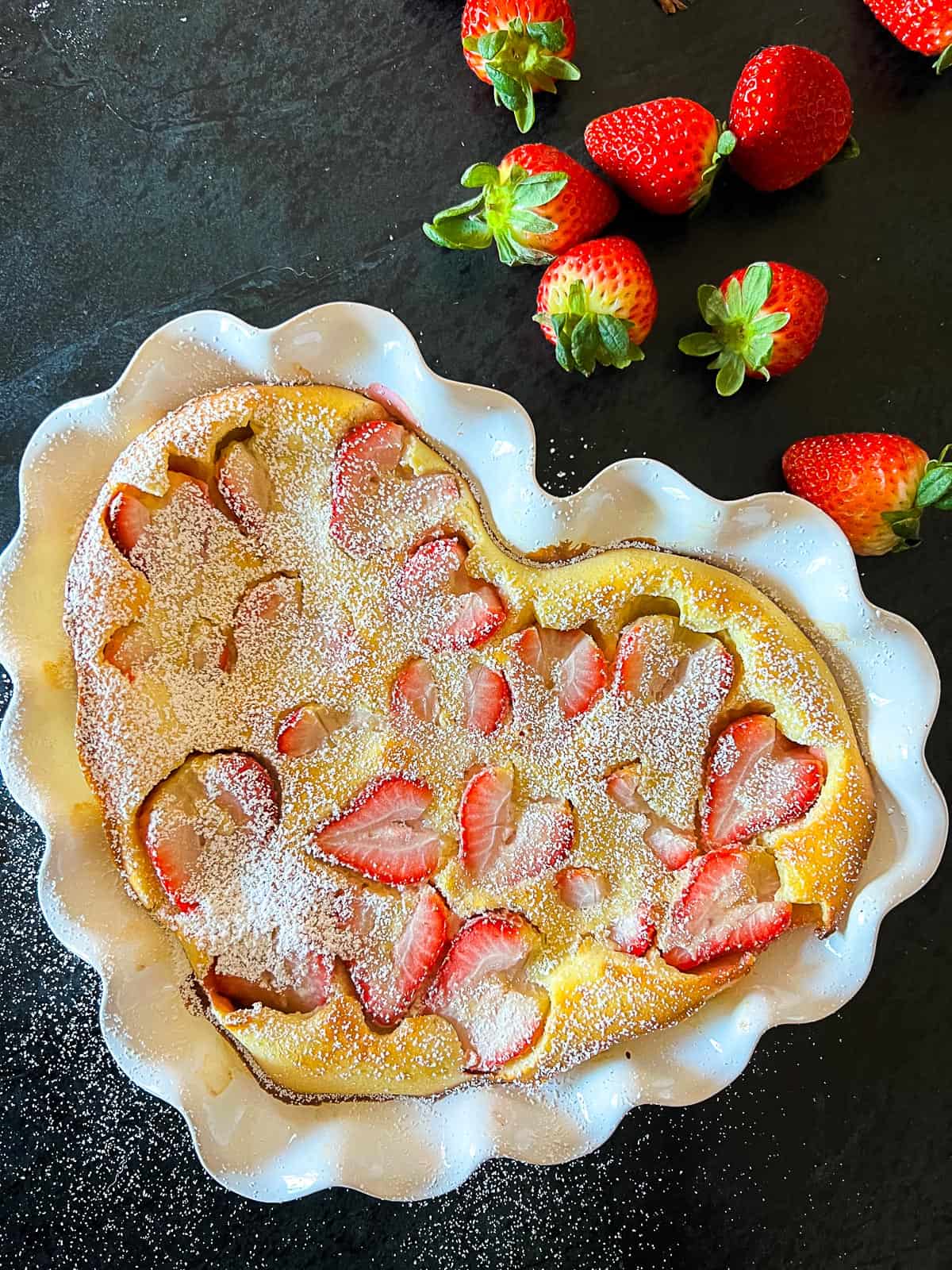 strawberry clafoutis recipe from scratch in a heart shaped pie dish with fresh strawberries sprinkled around