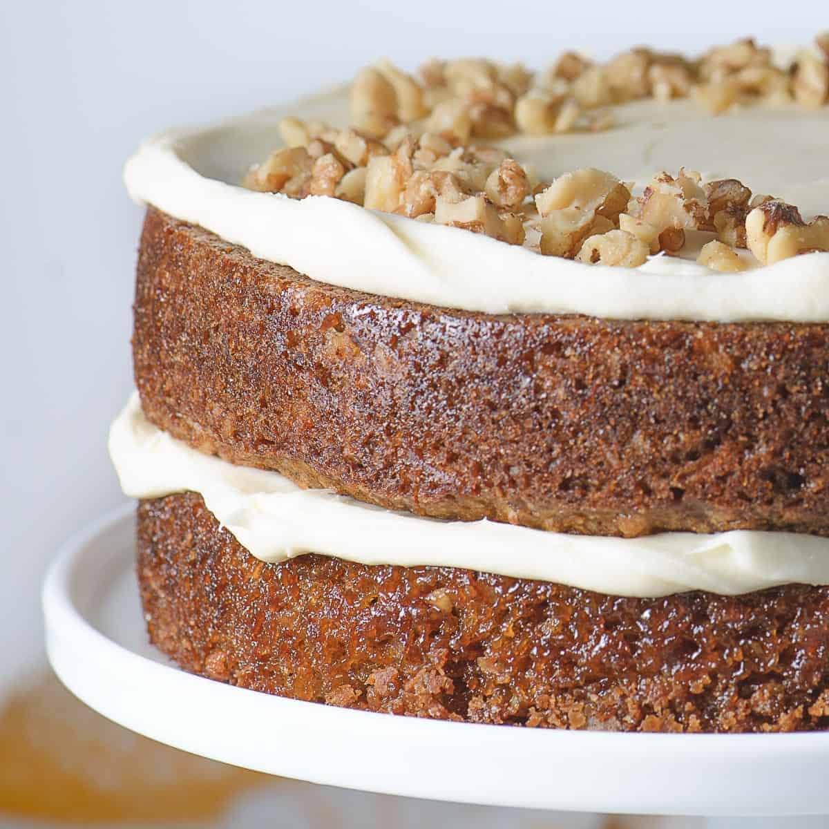 carrot cake layers friosting with cream cheese icing and topped with crushed walnuts