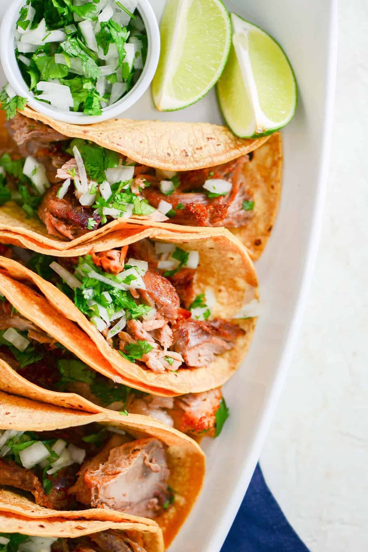 a platter of carnitas tacos dressed with cilantro, onions and lime.