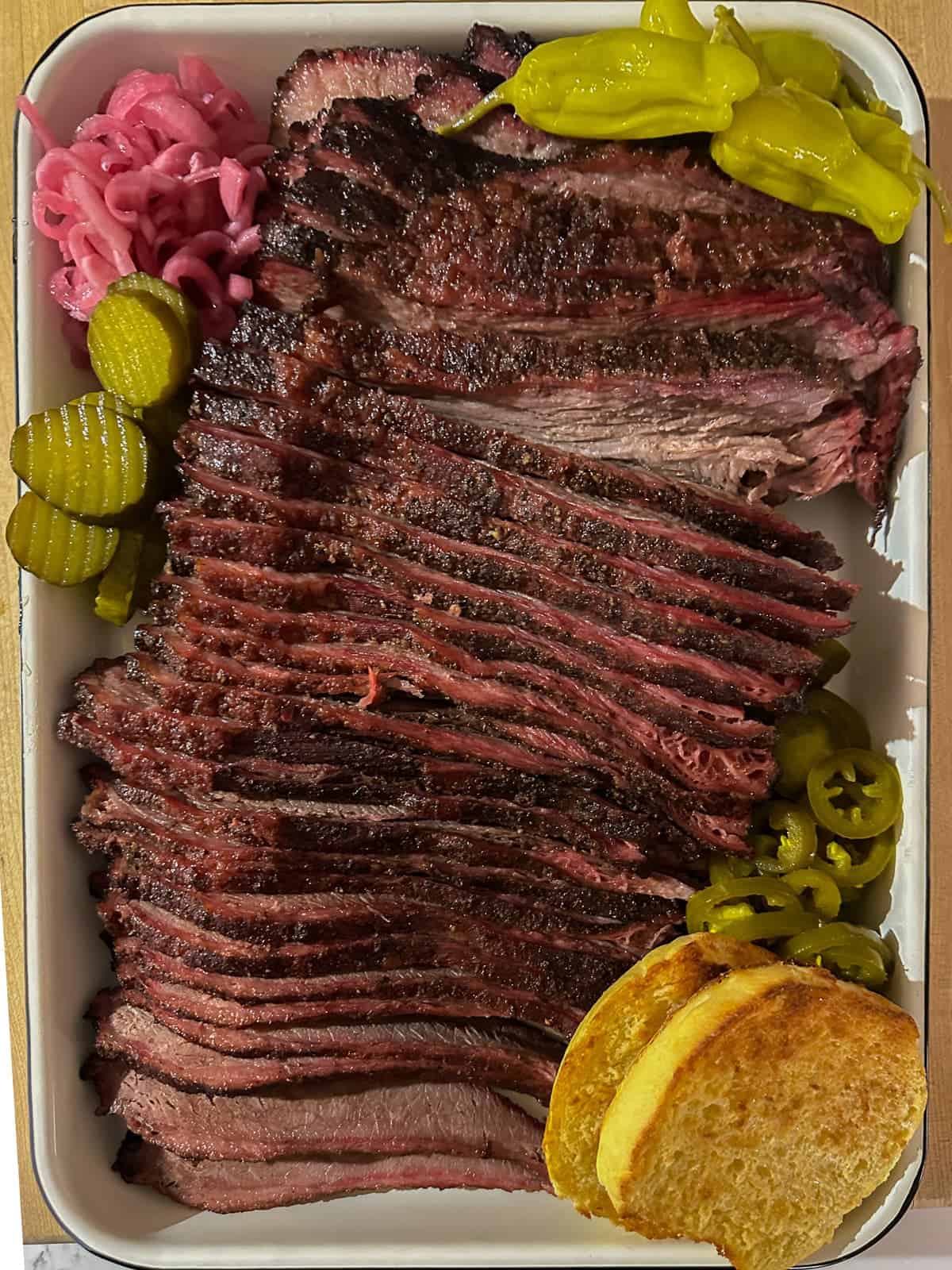 sliced smoked brisket served on a white pan with pickles and peppers