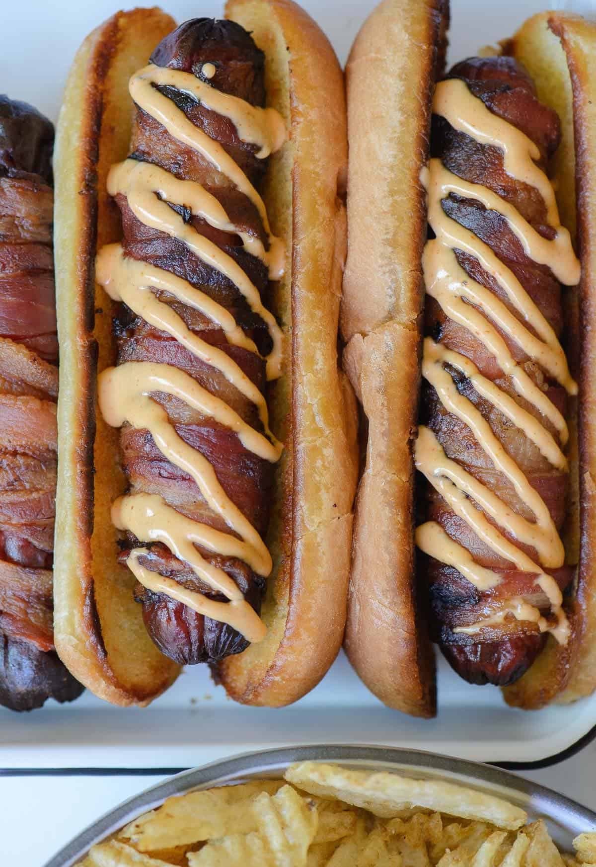 2 bacon wrapped hot dogs serve on toasted buns with spicy mayo