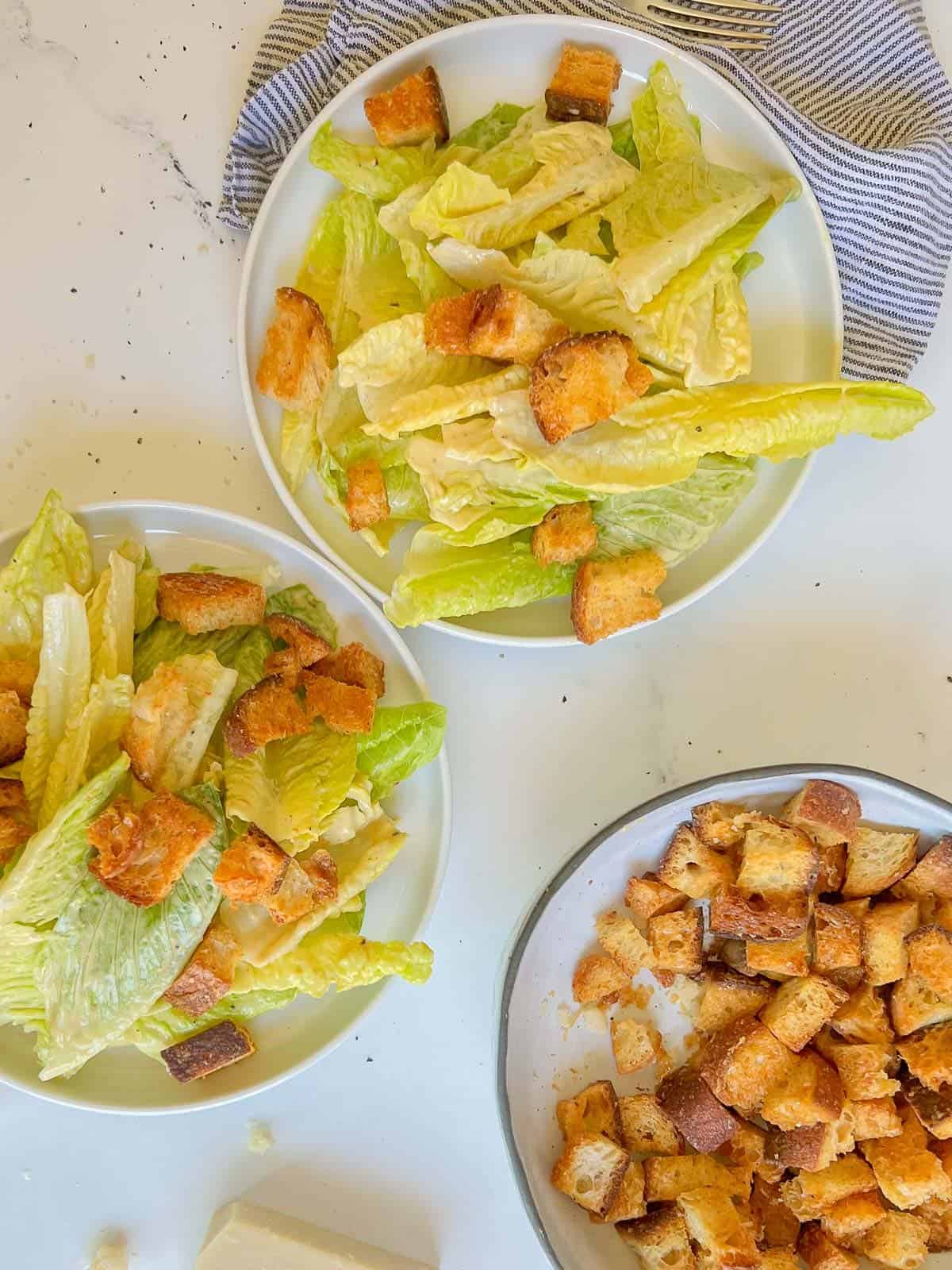 beautiful plates of caesar salad with a large bowl of homemade croutons on the side