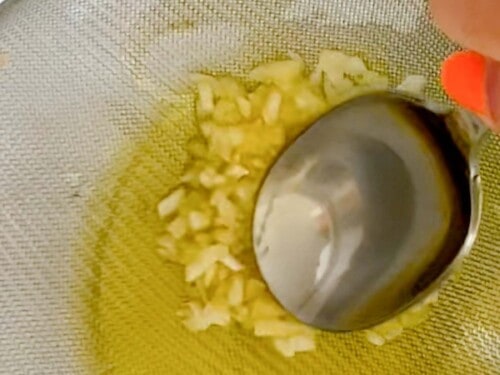 pressing garlic against a fine mess sieve with the back of a. spoon to squeeze out oil