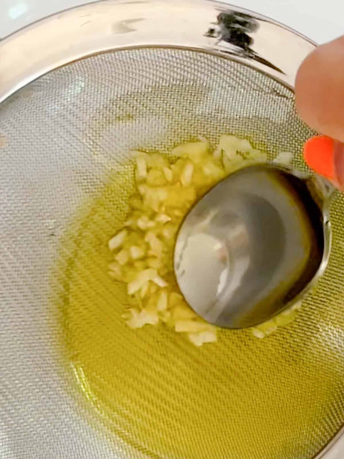 pressing garlic against a fine mess sieve with the back of a. spoon to squeeze out oil