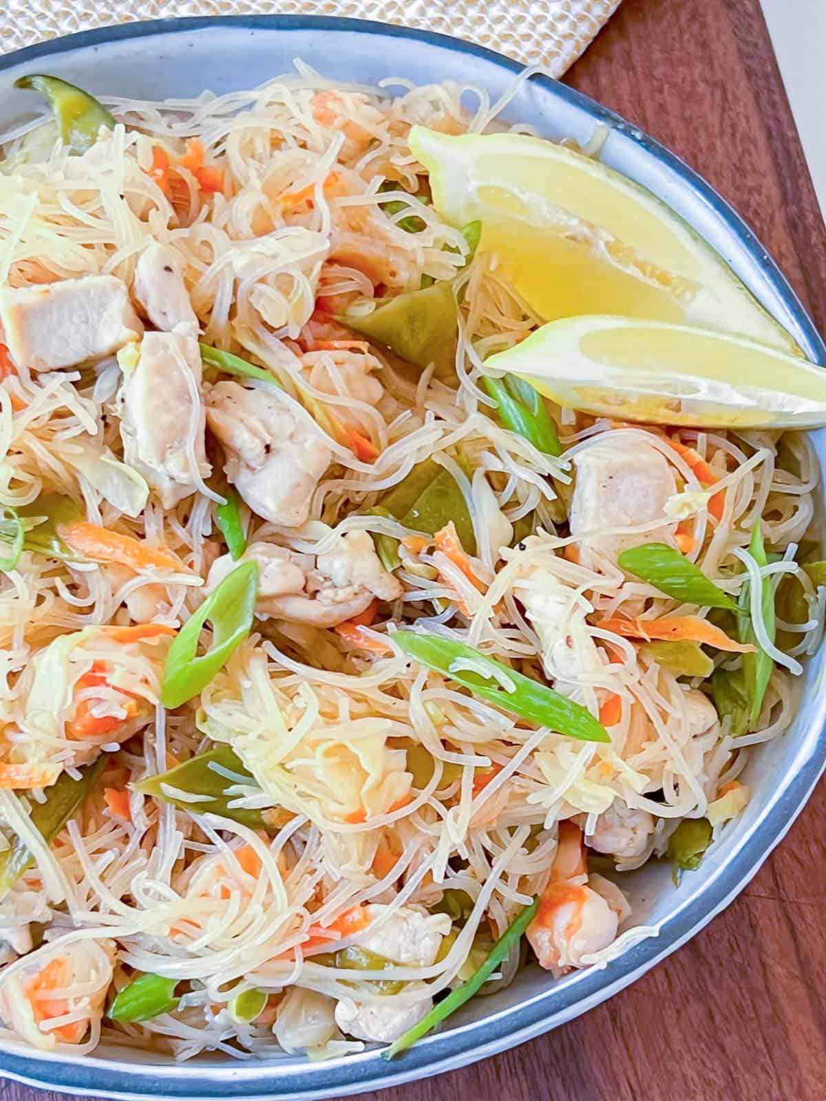 pancit bihon with shrimp and chicken in a white bowl served with lemon wedges