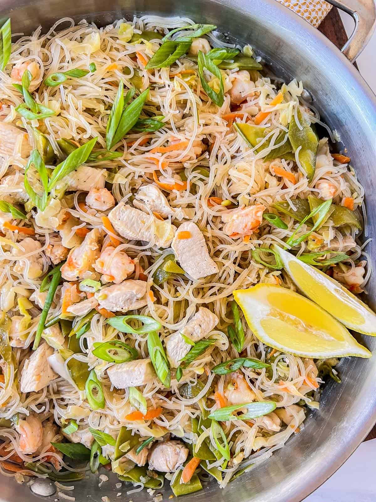 pancit bihon cooked in a large skillet, made with chicken, shrimp, and a savory broth