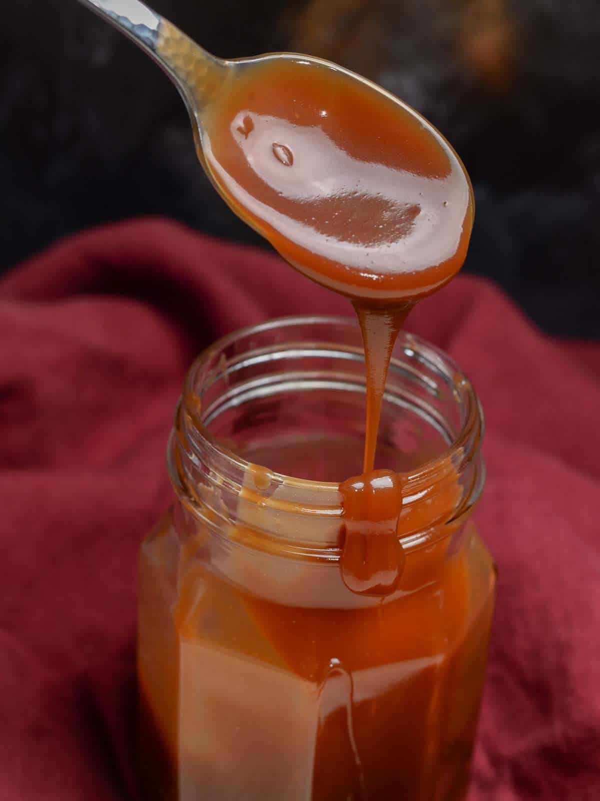 caramel sauce in a mason jar dripping off of a spoon