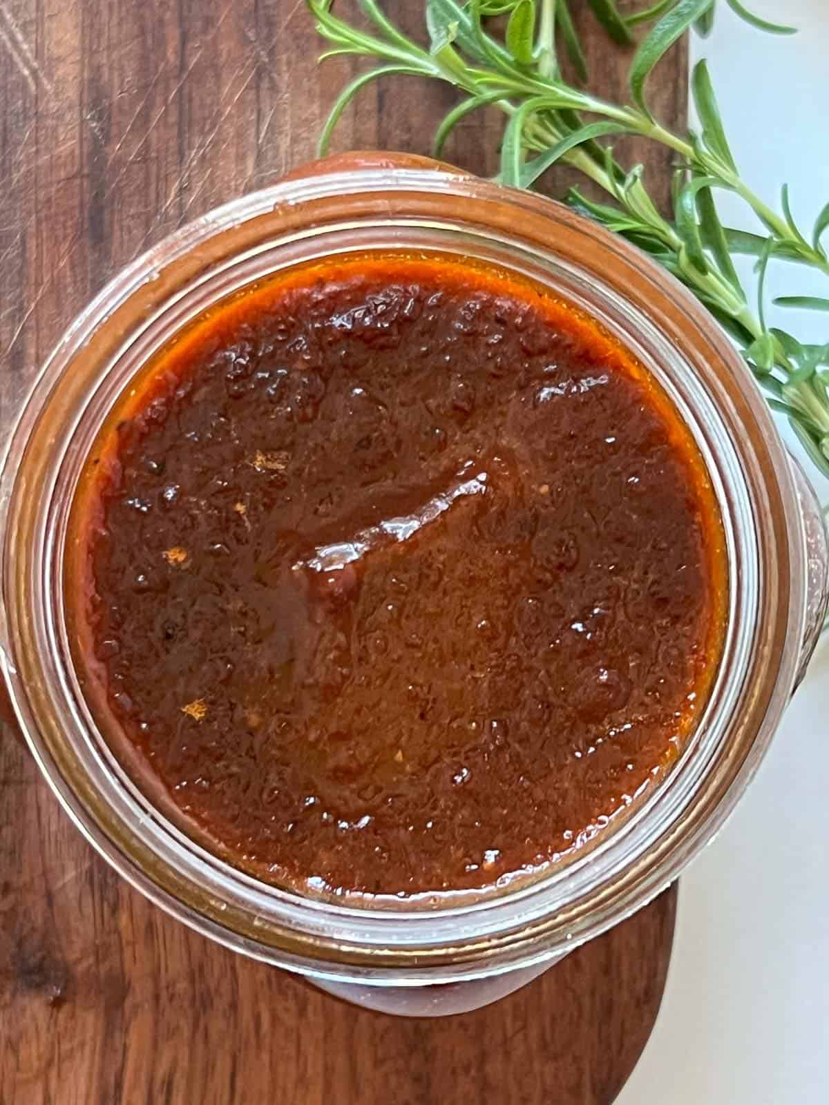 homemade bbq sauce in a mason jar sitting on top of a cutting board