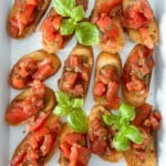 Simple tomato crostini recipe on a white platter. garnished with fresh basil.