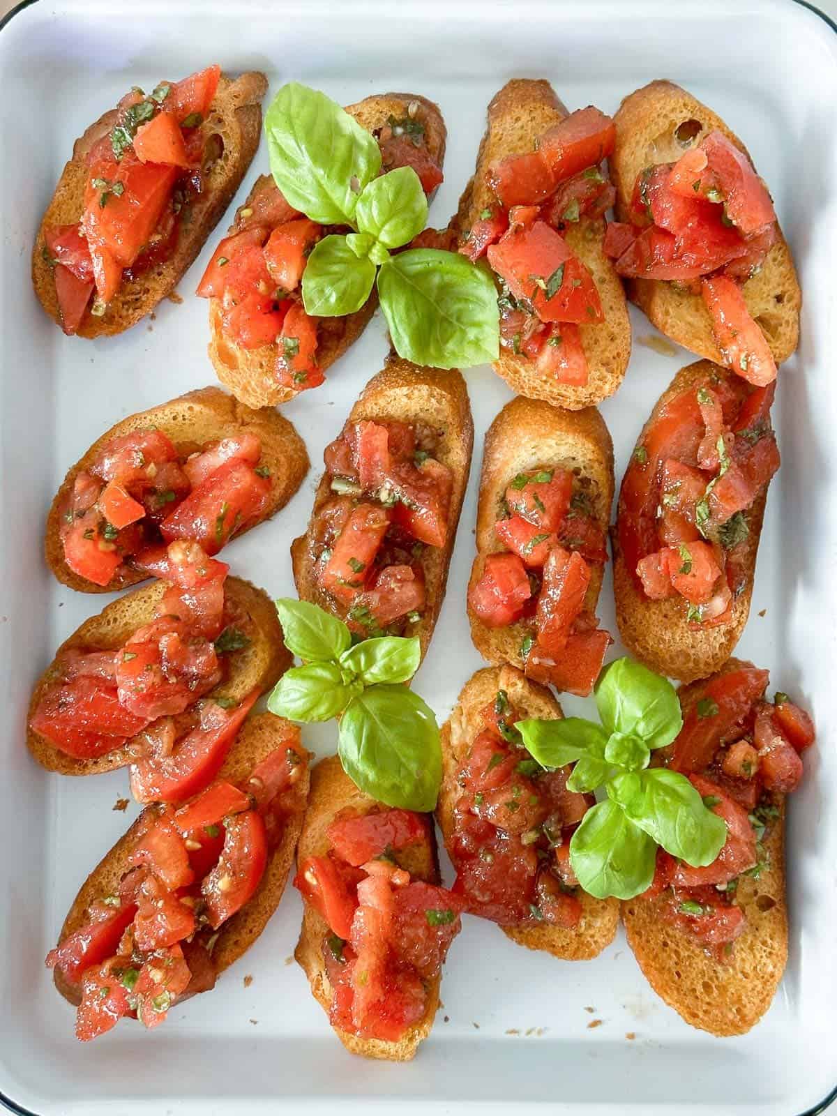 Simple tomato crostini recipe on a white platter. garnished with fresh basil.