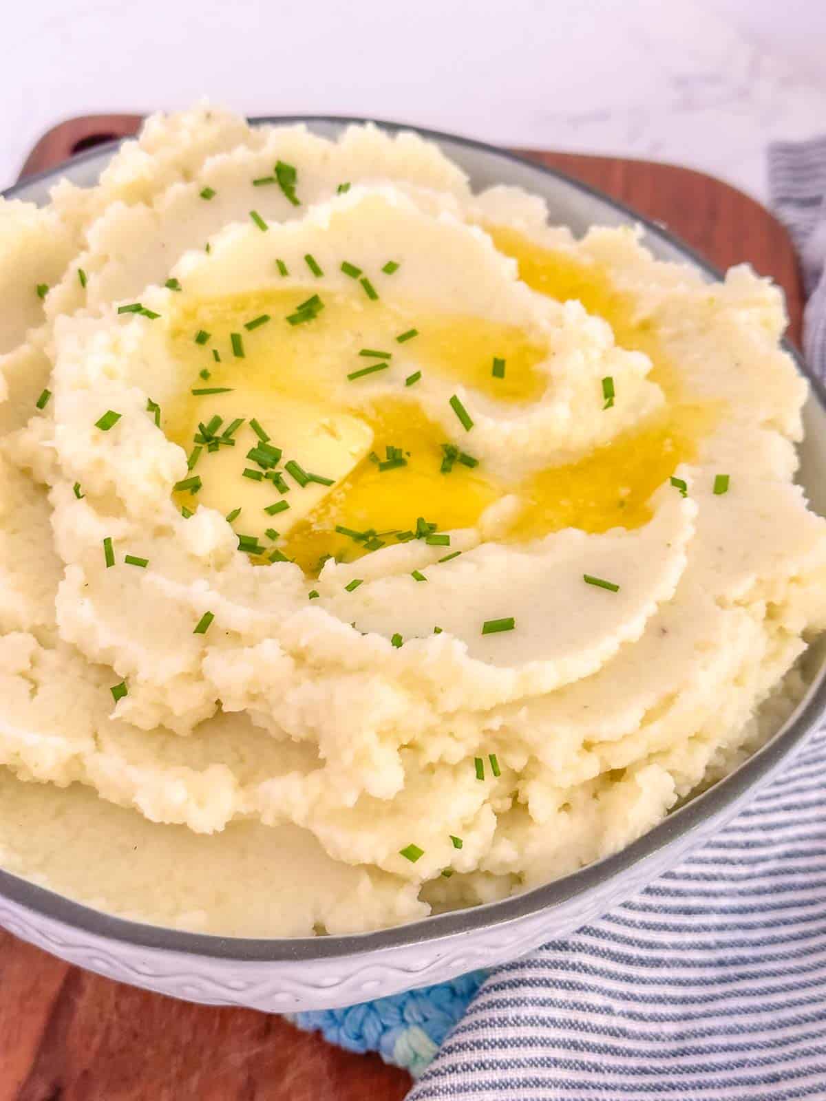 creamy cauliflower mash with butter and chives in a white serving bowl