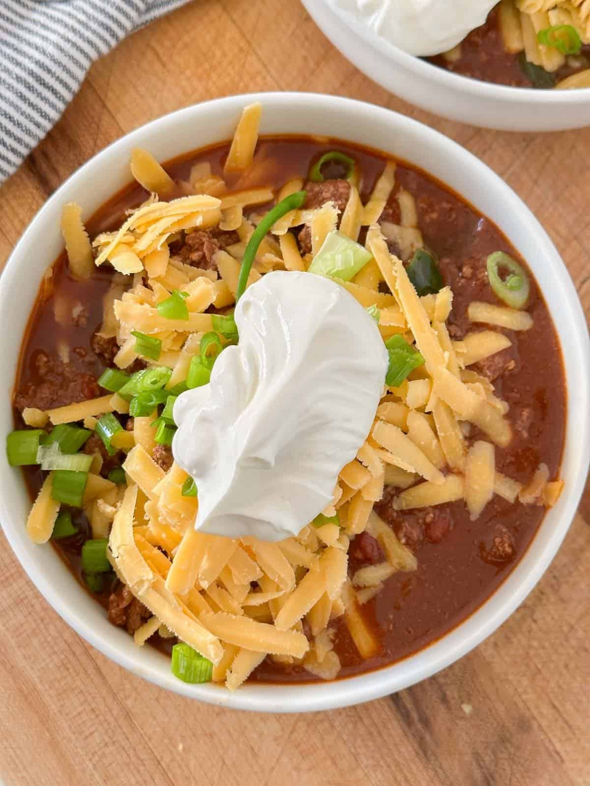 a bowl of keto chili topped with shredded cheese, sour cream and green onions