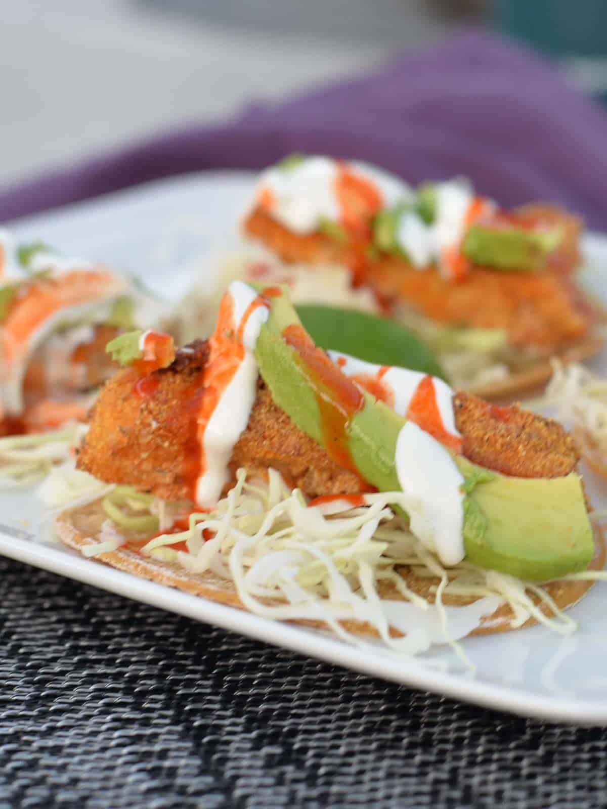 fish tacos on a white plate, topped with mexican slaw, avocado and lime crema
