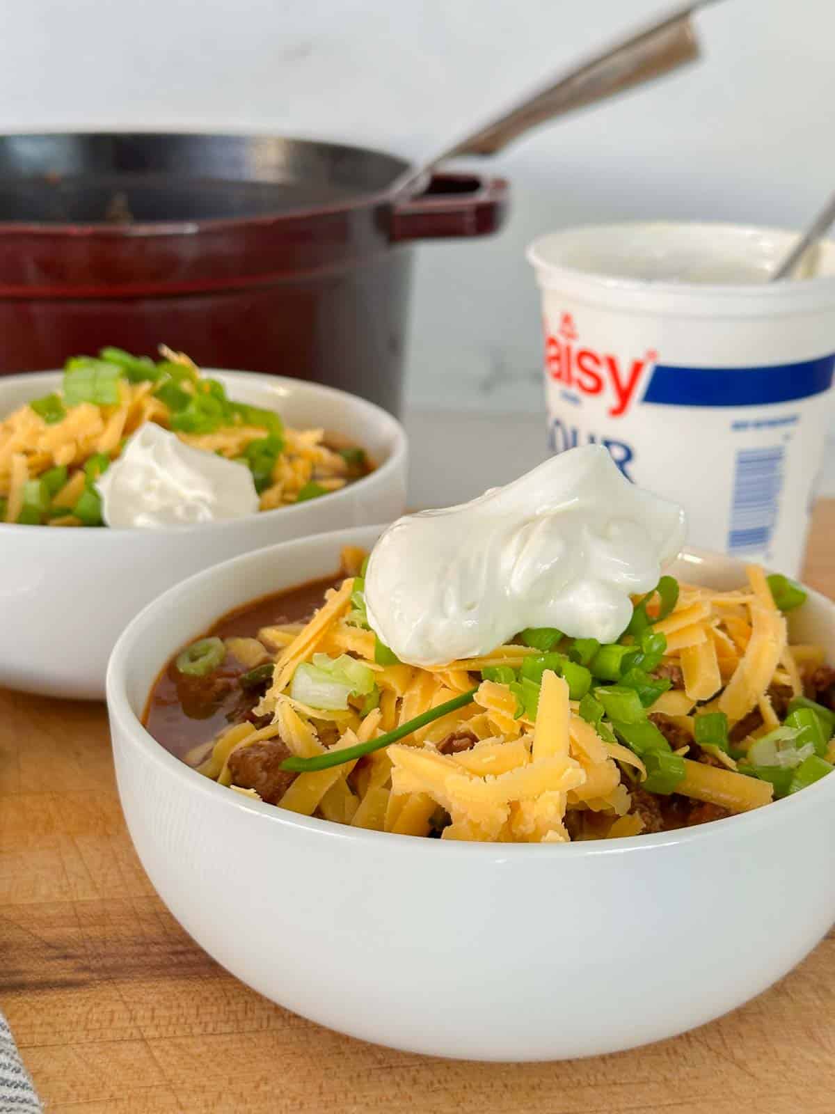 two bowls of keto chili dressed with all the toppings, sour cream, cheddar, and green onions