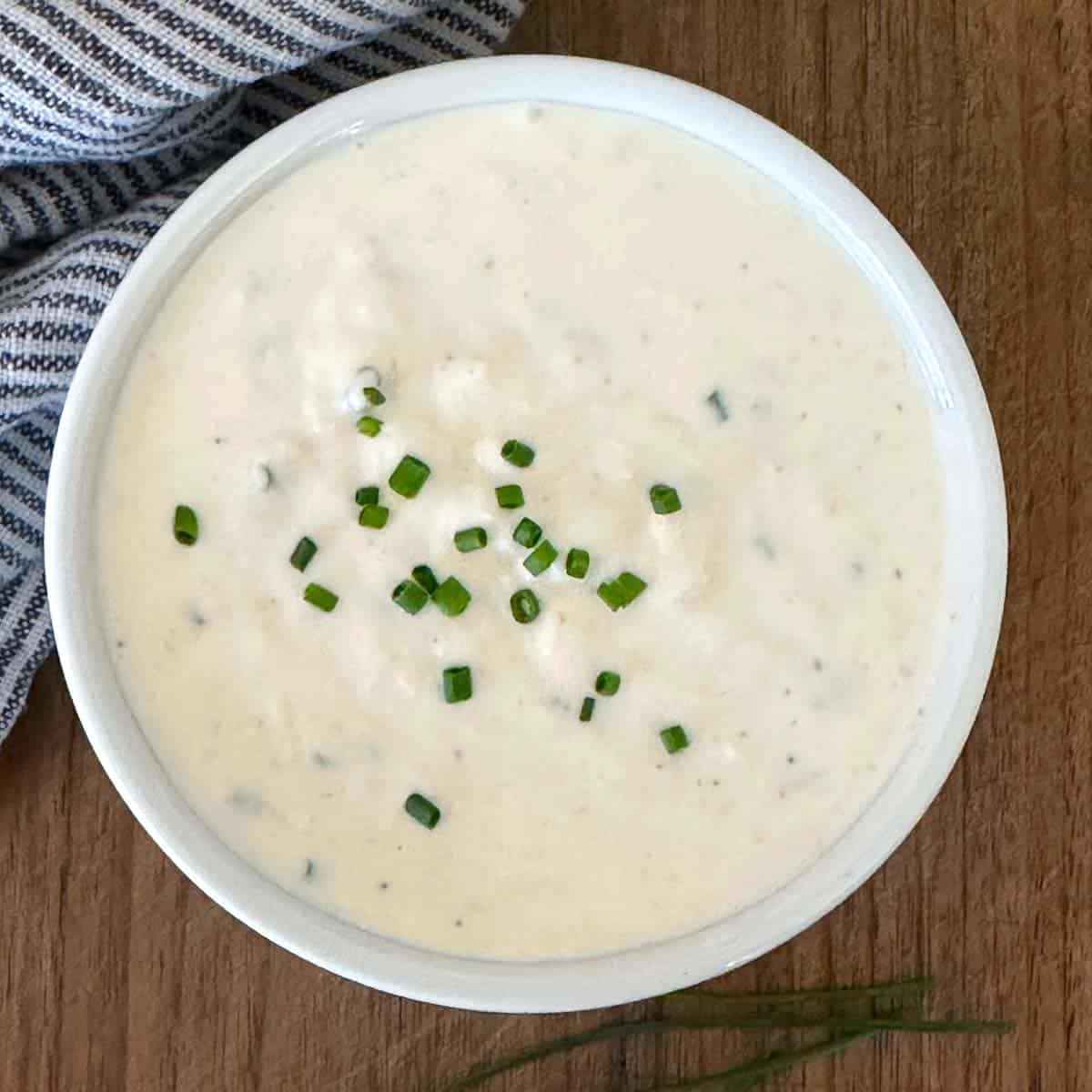 homemade horseradish cream sauce pictured with a striped napkin and fresh chives