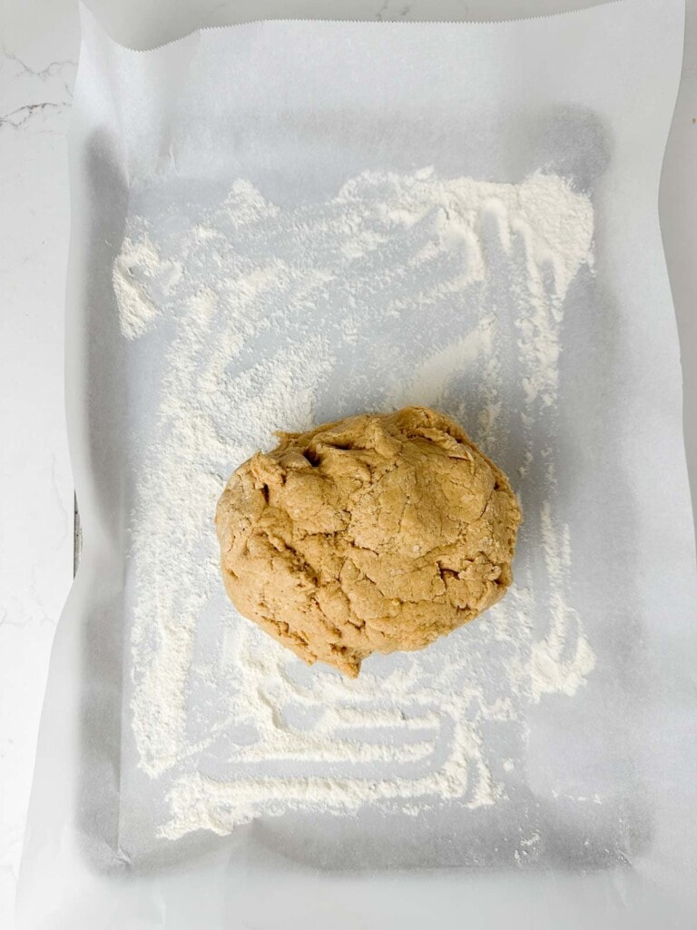 apple cider donut dough on a parchment lined baking sheet, ready to be pressed out