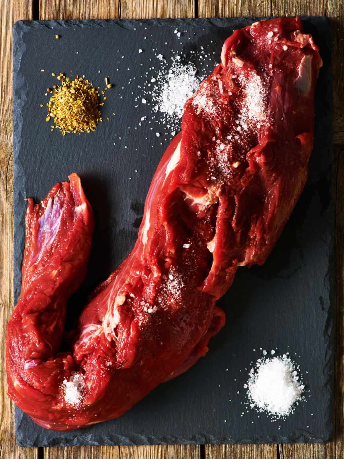 full sized beef tenderloin roast on a black slate board