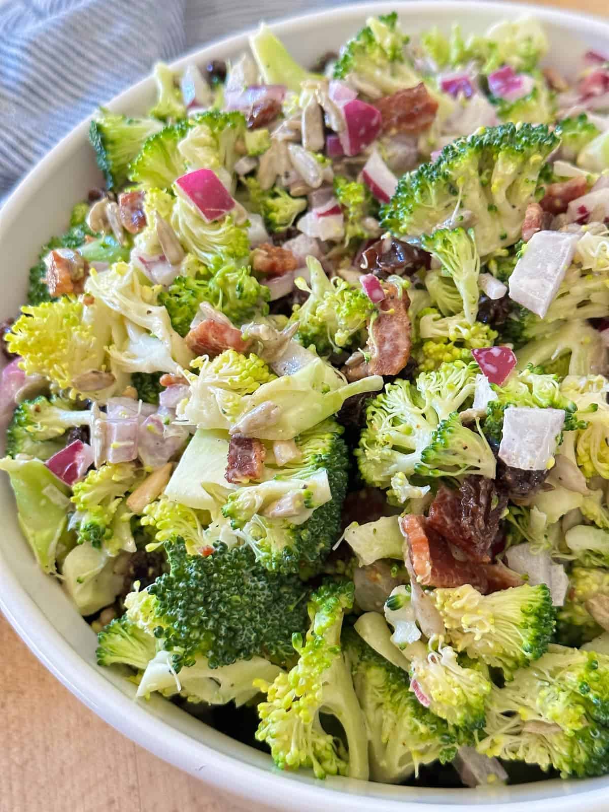 the classic broccoli salad in a white serving bowl. Zoomed into see all the ingredients closer.