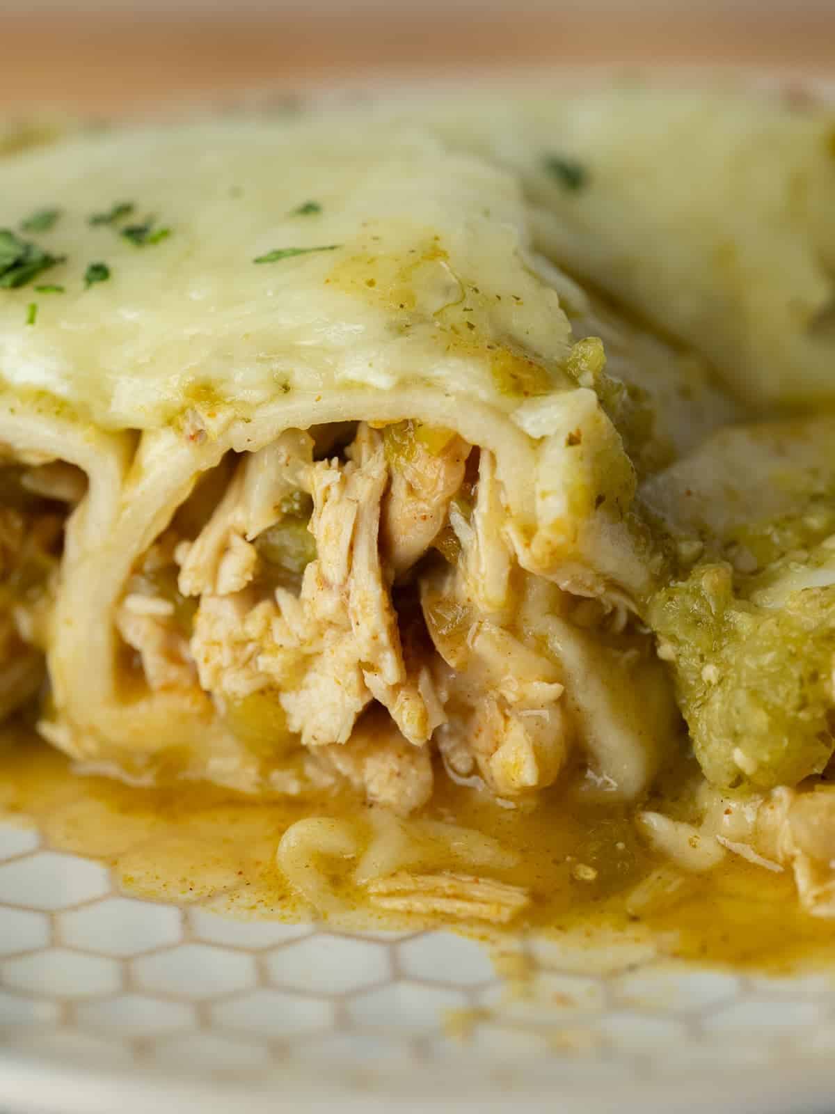 cheesy saucey enchiladas verde on a plate showing the shredded chicken filling