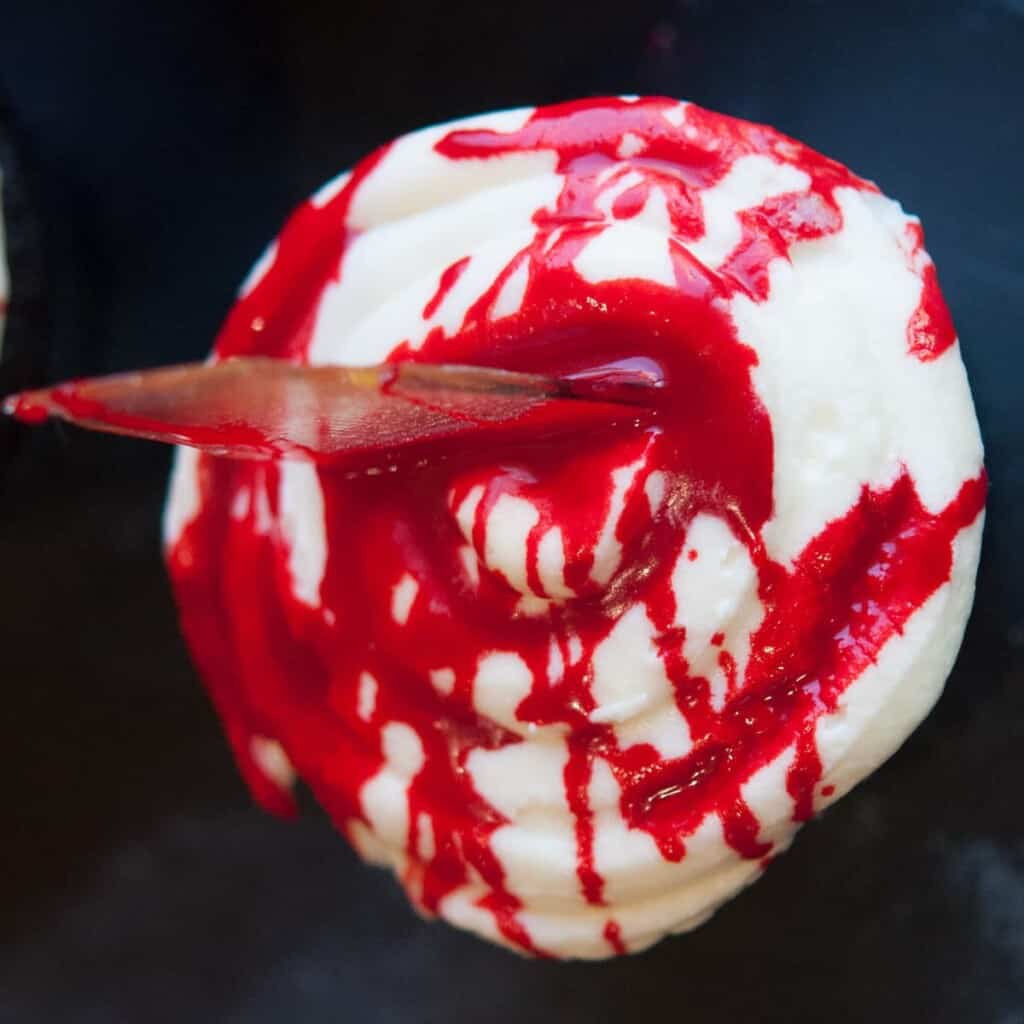 halloween cupcake with cream cheese frosting, edible blood and a sugar glass shard stabbed into the top