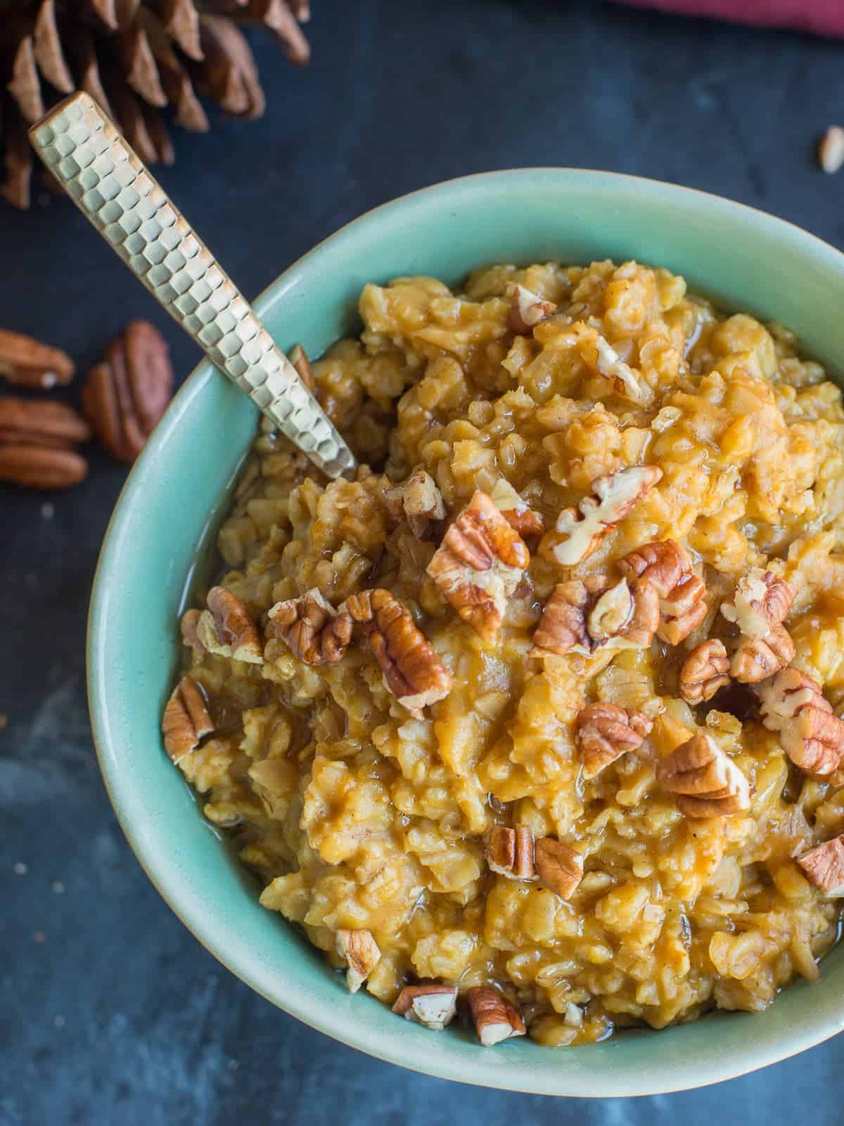 a bowl of steaming pumpkin oatmeal topped with pecans and a drizzle of maple syrup