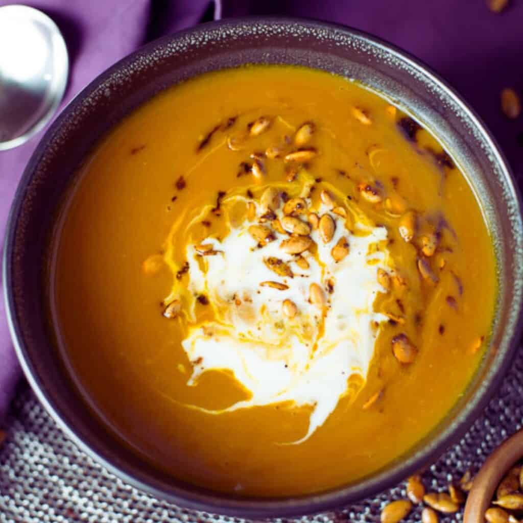 a bowl of vegan pumpkin soup with toasted pepitas and creme fraiche served in a black bowl