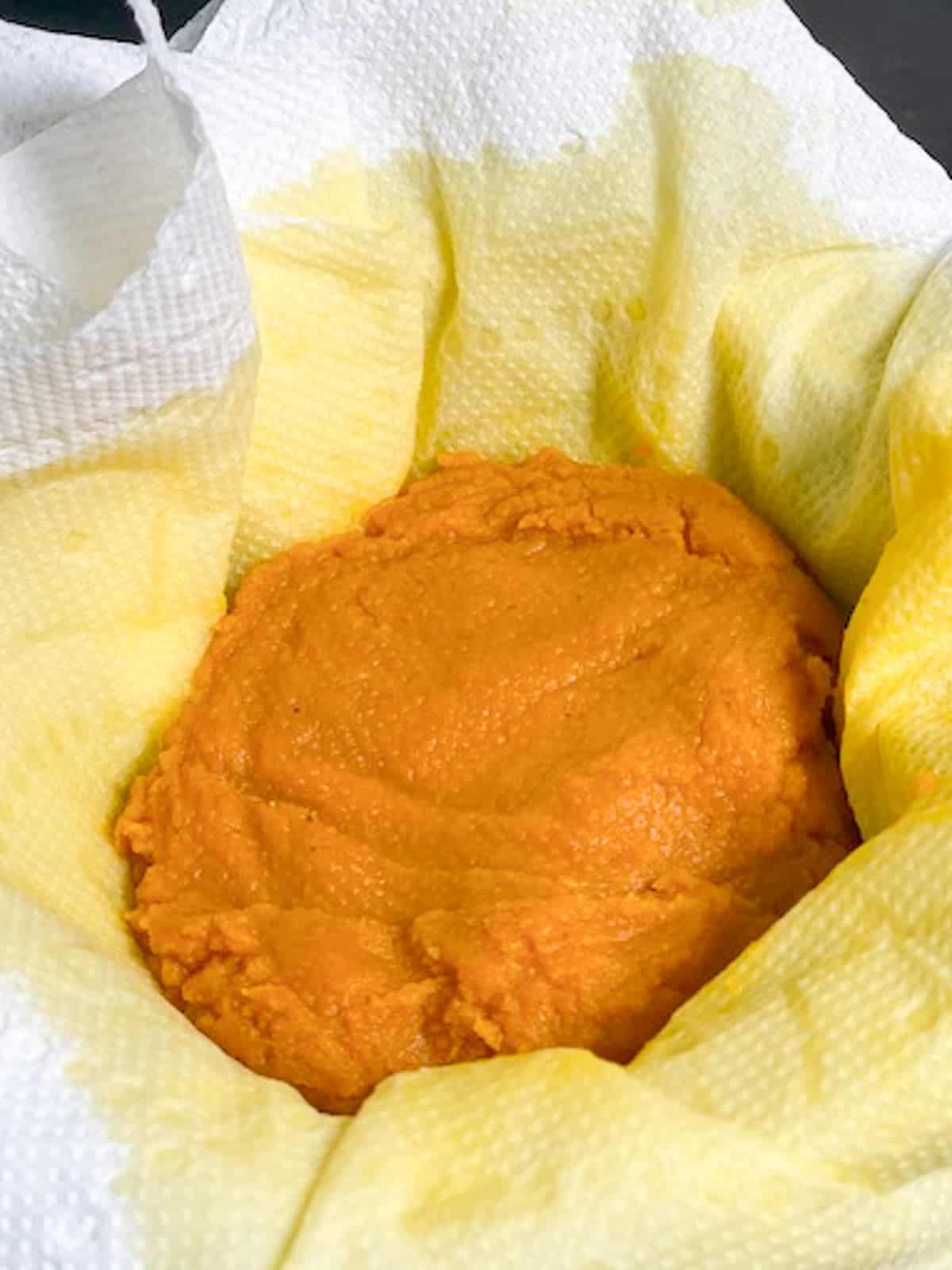 straining pumpkin puree in a paper towel lined fine seive to eliminate excess moisture