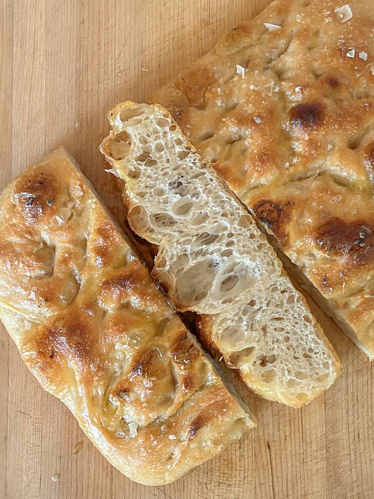 slices of focaccia bread on a cutting board to show the huge bubbles inside the chewy bread