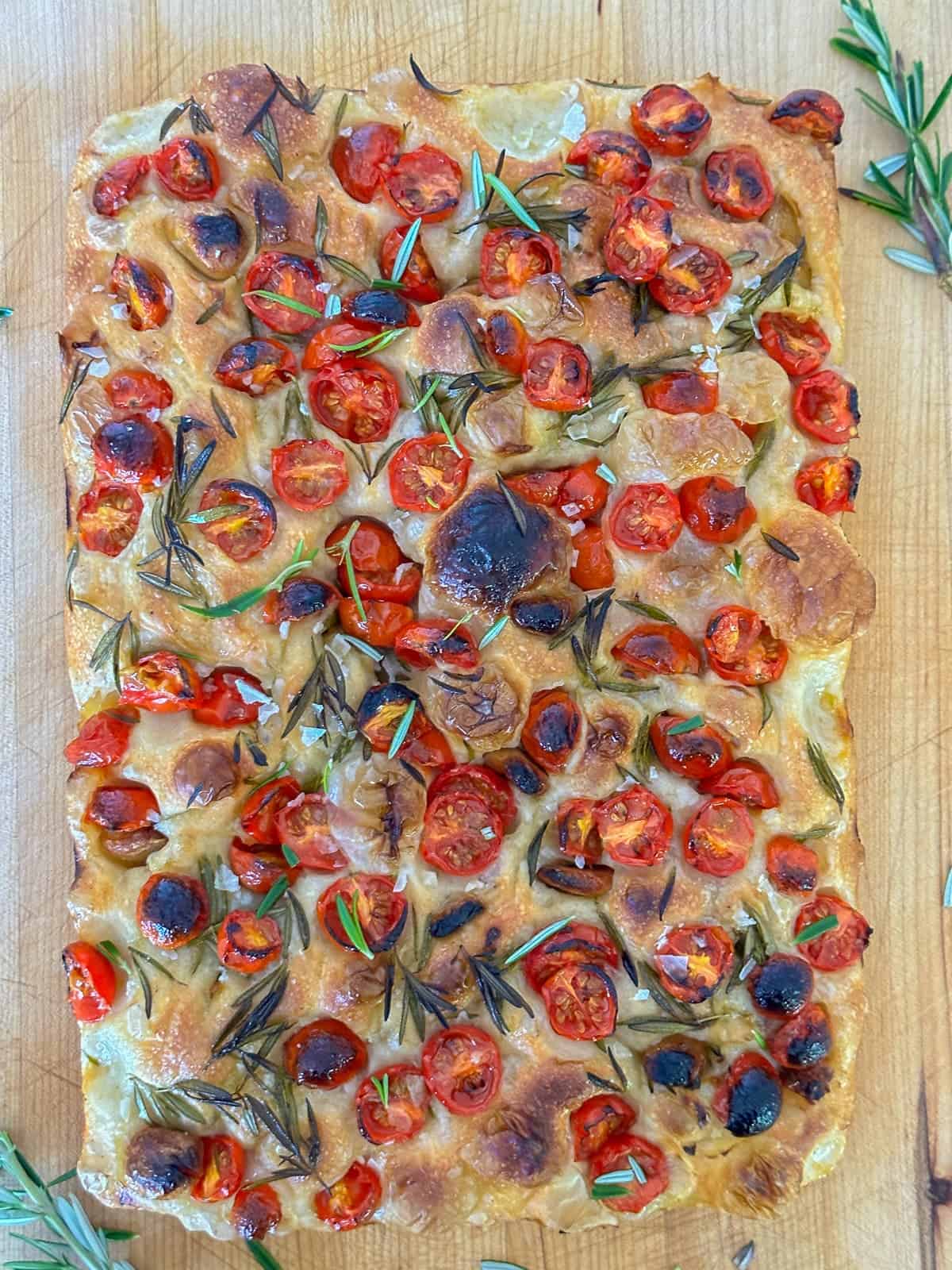 a loaf of freshly baked tomato focaccia bread resting on a cutting board.
