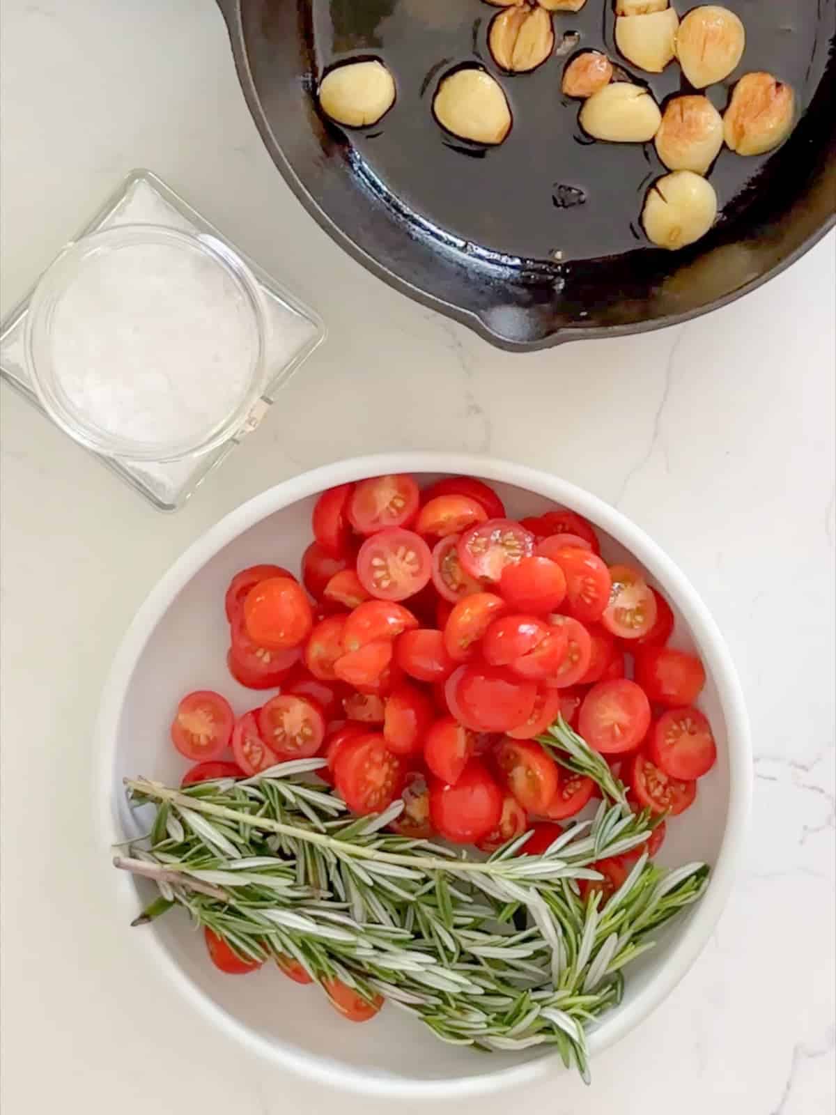 ingredients used to top tomato focaccia bread. including; roasted garlic, cherry tomatoes, rosemary, and flaky sea salt